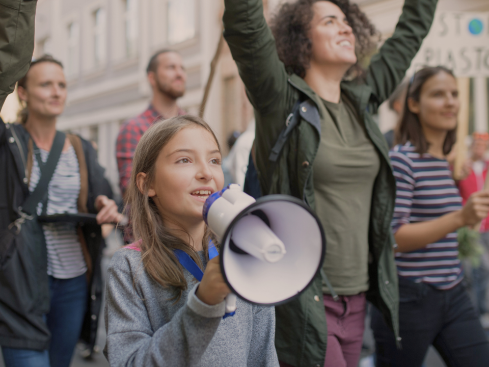 Une foule manifeste, une enfant parle dans un mégaphone.