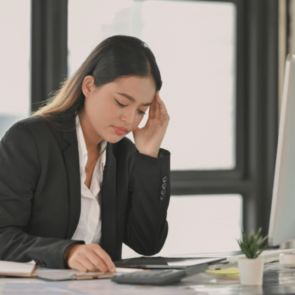 Une femme, visiblement préoccupée, se tient la tête en lisant le contenu affiché sur sa tablette, posée sur son bureau.