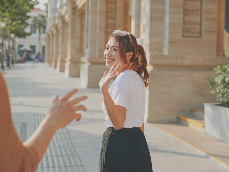 Une femme fait un signe d'au revoir à quelqu'un dans la rue.