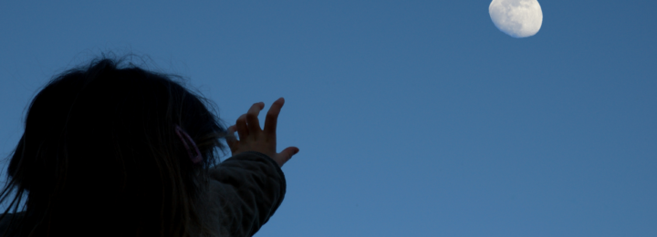 Une fillette tend le bras pour toucher la lune.