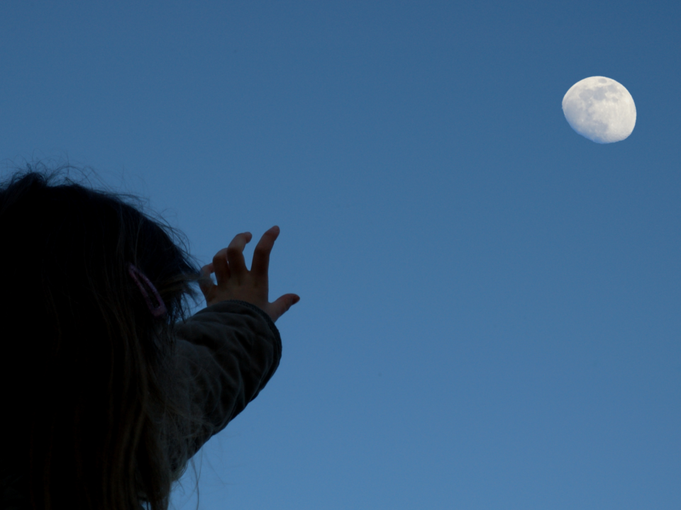 Une fillette tend le bras pour toucher la lune.