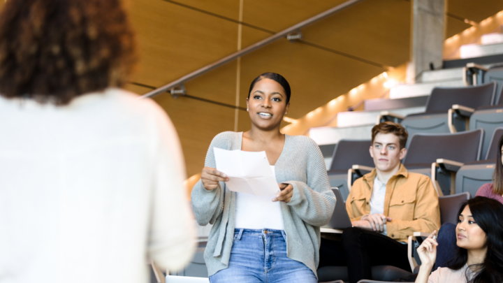 Une étudiante s’exprime à l’oral devant une classe en amphithéâtre.