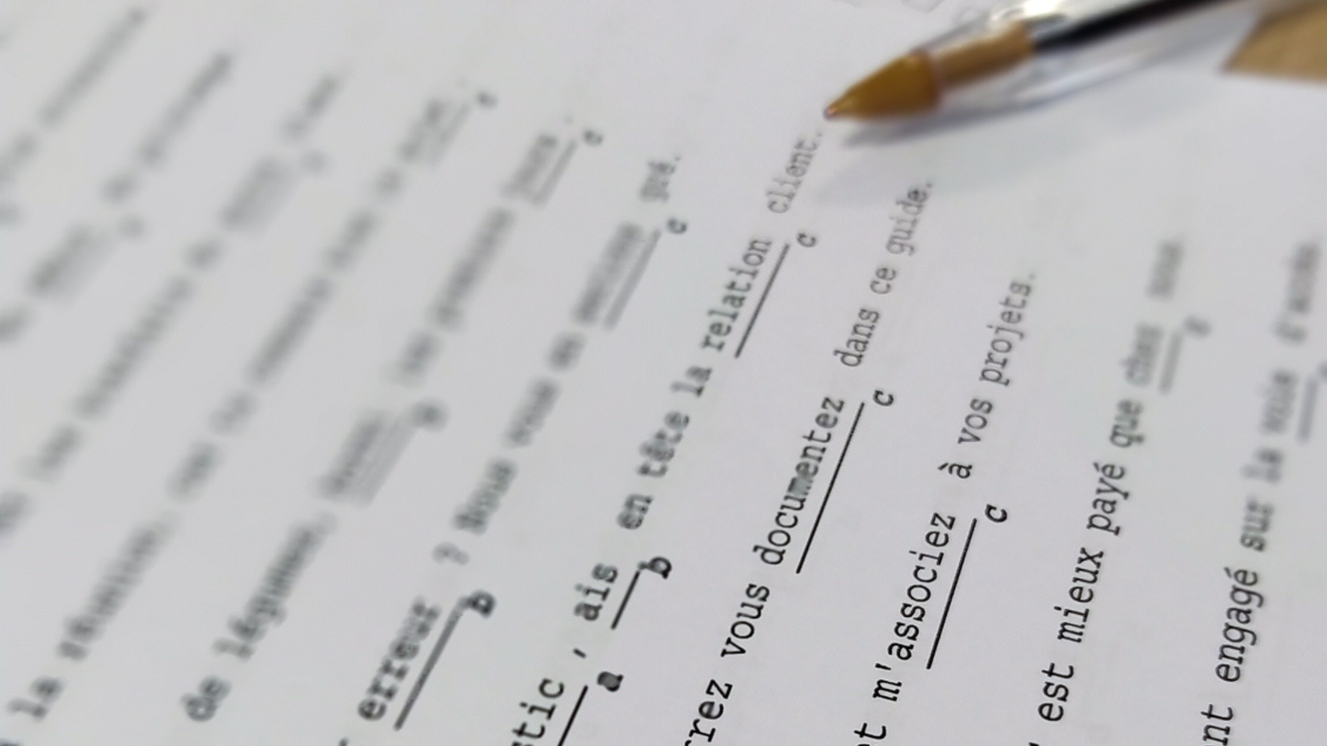 Gros plan sur un test de langue française avec des phrases à trous et des choix multiples, accompagné d’un stylo transparent.