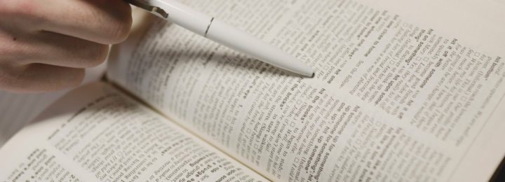 Une personne lit un dictionnaire et s'aide d'un stylo pour ne pas sauter de ligne.