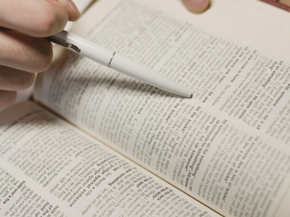 Une personne lit un dictionnaire et s'aide d'un stylo pour ne pas sauter de ligne.