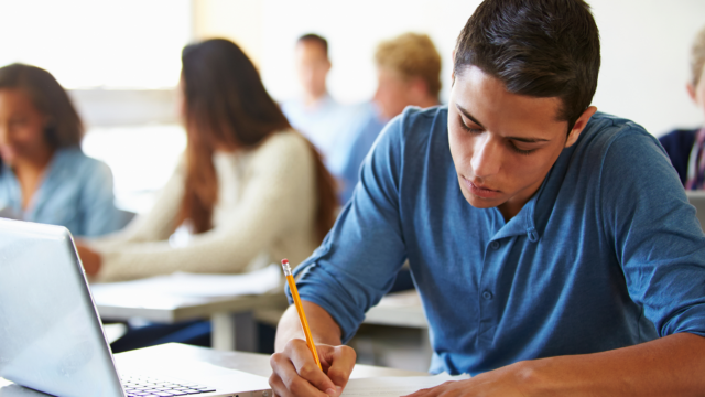 Un élève concentré rédige un devoir en classe