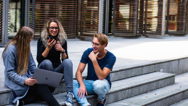 Trois étudiants assis sur des marches d’escalier devant leur établissement